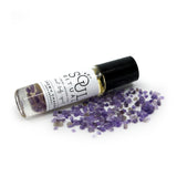 Crown Chakra roller bottle laying on crushed purple amethyst. Soul Ritual charka roller collection for crown chakra infused with reiki, amethyst crystals, and essential oils for your energetic well-being,