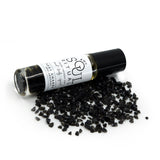 Root Chakra roller bottle laying on crushed black obsidian gemstones. Soul Ritual chakra roller bottle collection for root chakra infused with reiki, black obsidian and chakra essential oil blend for your energetic well-being,